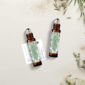 Two amber glass roller ball bottles of No. 12 Pistachio Gelato luxury perfume oil by Pleasant Run Farms, with sage green floral labels, on a cream surface surrounded by fresh herbs